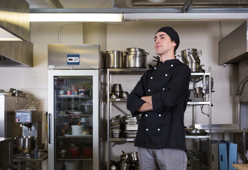 Kaip išsirinkti restoranų įrangą: nuo virtuvės iki baro zonos Profesionali restorano virtuvės įranga su šefu prie viryklės ir veikiančia baro zona, atspindinti sklandų darbo procesą.