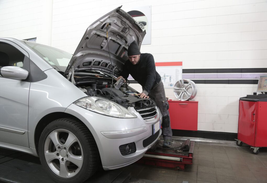 Automobilių serviso meistras apžiūri automobilio stabdžių, pakabos ir variklio komponentus, vertindamas nusidėvėjimą ir techninę būklę.